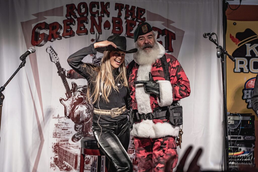 Performer in a cowboy hat posing on stage with Santa wearing a green beret at Rock the Green Beret