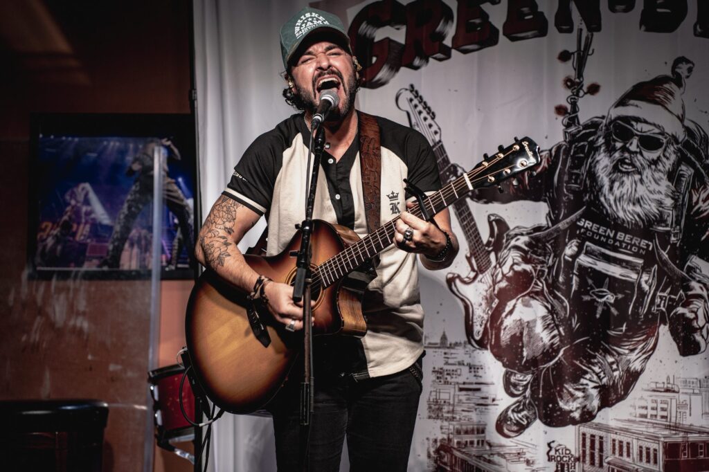 Singer performing with an acoustic guitar in front of the Rock the Green Beret banner